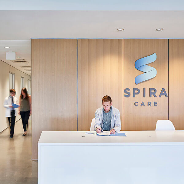 A young man sitting at the front desk of a Spira Care health center.
