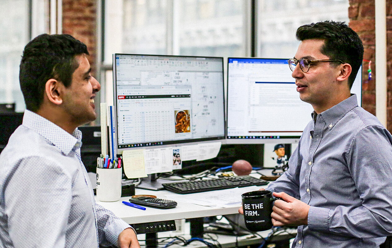 Two engineers standing at a work station chatting in the New York office.