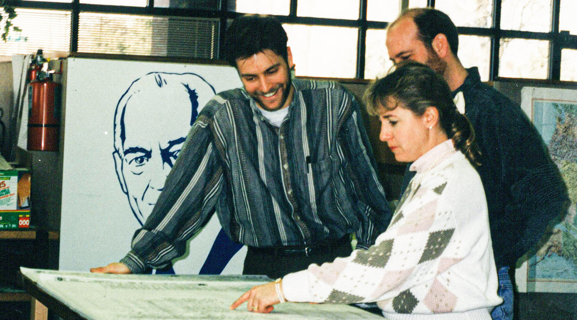 Group of three engineers reviewing engineering plans in the office from the 1990's.